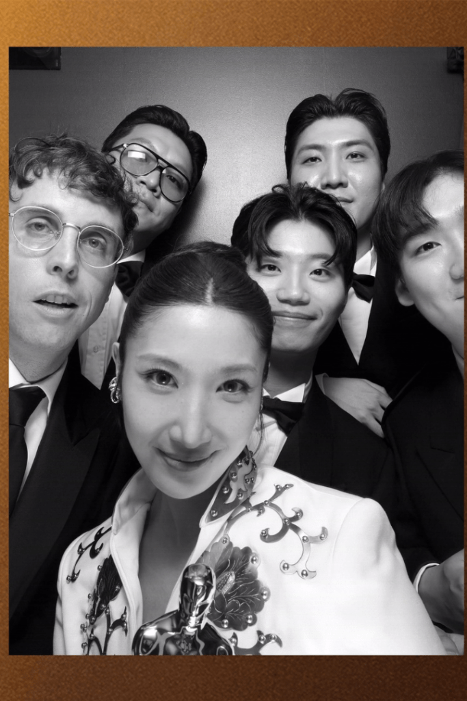 Group selfie of filmmakers in formal attire holding an Oscar statuette at the Academy Awards"